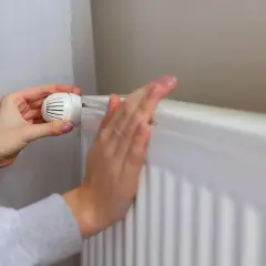 Dłonie regulują termostat grzejnika. Czas na sezon grzewczy od jesieni do wiosny.