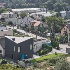 Nowoczesny dom o trójkątnym kształcie na tle zabudowy jednorodzinnej. Widać tu typowe **grunty rolne zabudowane**, z domami, szklarniami i zielenią.