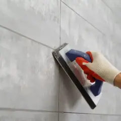 Ręka w rękawicy nakłada fugę epoksydową na zewnątrz na szare płytki.