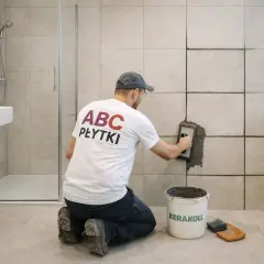 Mężczyzna kładzie fugę epoksydową na płytkach w łazience. Pokazuje, jak kłaść fugę, by uzyskać trwały efekt.