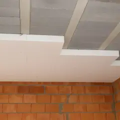 Ocieplenie stropu styropianem w trakcie budowy. Widoczne ceglane ściany i betonowy strop z elementami izolacji.