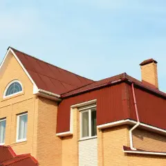 Dom z cegły z czerwonym dachem, okna i komin. Widoczna mansarda, czyli przestrzeń pod dachem.