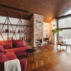 Przytulny salon w stylu wiejskim z ceglanym kominkiem, czerwoną kanapą i drewnianą podłogą.