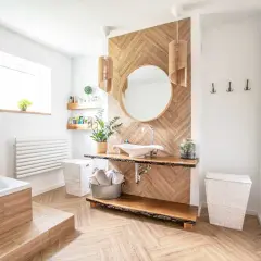 Drewniane panele w jodełkę to świetny pomysł na to, co na ściany w łazience. Uzupełnia je okrągłe lustro i umywalka nablatowa.