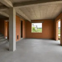 Wnętrze domu w stanie surowym z ceglanymi ścianami, betonowymi stropami i schodami.