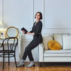 Kobieta w eleganckim, prążkowanym stroju siedzi na kanapie, trzymając książkę. To kwintesencja stylu glamour – wyrafinowanie i blask.