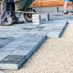 Układanie betonowych płyt na żwirze. Pracownicy tworzą nowoczesny taras, gdzie beton zamiast kostki nadaje mu minimalistyczny charakter.