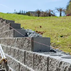 Budowa murek oporowy z bloczków betonowych, najtaniej i solidnie. Widać drabinę i sznur geodezyjny.