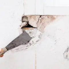 Dłonią z kielnią usuwa się luźny tynk, przygotowując ścianę do wypełnienia dużych ubytków.