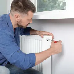 Mężczyzna odpowietrza grzejnik żeliwny, używając śrubokręta.