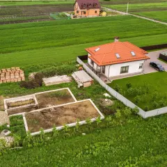 Budowa domu na działce z fundamentami, materiałami budowlanymi i gotowym budynkiem obok. Minimalna powierzchnia działki budowlanej widać na przykładzie.