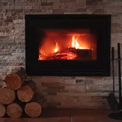 Płonący kominek z drewnem, stos drewna i akcesoria kominkowe.