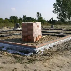 Fundamenty budynku w stanie zero, z widocznymi zarysami ścian i stosem cegieł.