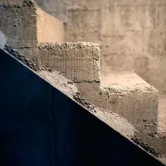 Surowe, betonowe schody wewnętrzne czekają na wyrównanie. Widać nierówności i siatkę zbrojeniową.