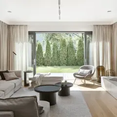 Przytulny salon w stylu hygge wnętrza. Jasne meble, miękkie tkaniny i widok na zielony ogród tworzą atmosferę spokoju.