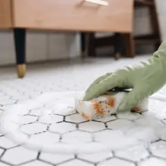 Rękawiczka w zielonej gumie czyści pianą błyszczące kafelki heksagonalne.