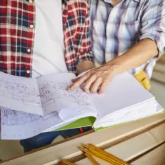 Dwóch budowlańców analizuje plany, omawiając nowelizację prawa budowlanego.