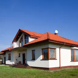 Nowy dom z białym tynkiem i czerwonym dachem. Elewacja domu wzory podkreślają jego nowoczesny charakter.