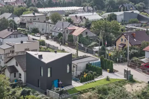 Nowoczesny dom o trójkątnym kształcie na tle zabudowy jednorodzinnej. Widać tu typowe **grunty rolne zabudowane**, z domami, szklarniami i zielenią.