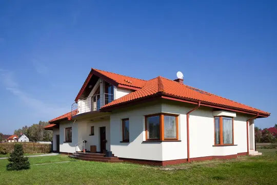 Nowy dom z białym tynkiem i czerwonym dachem. Elewacja domu wzory podkreślają jego nowoczesny charakter.
