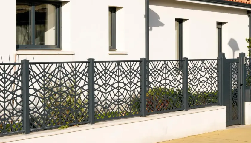 Nowoczesne, ciekawe ogrodzenia posesji z metalowymi panelami o geometrycznym wzorze liści. Elegancko oddzielają dom od ulicy.