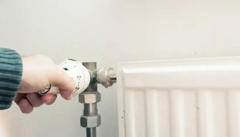 Dłoń reguluje termostat grzejnika. Po odpowietrzeniu zimny grzejnik w końcu zacznie grzać.