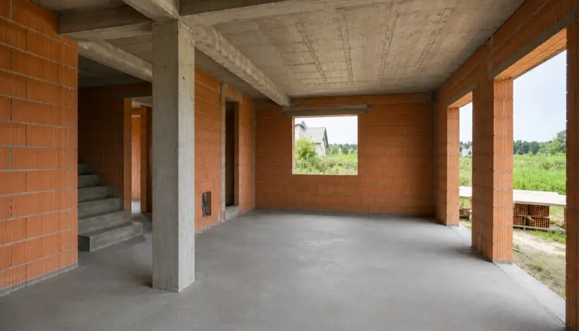 Wnętrze domu w stanie surowym z ceglanymi ścianami, betonowymi stropami i schodami.