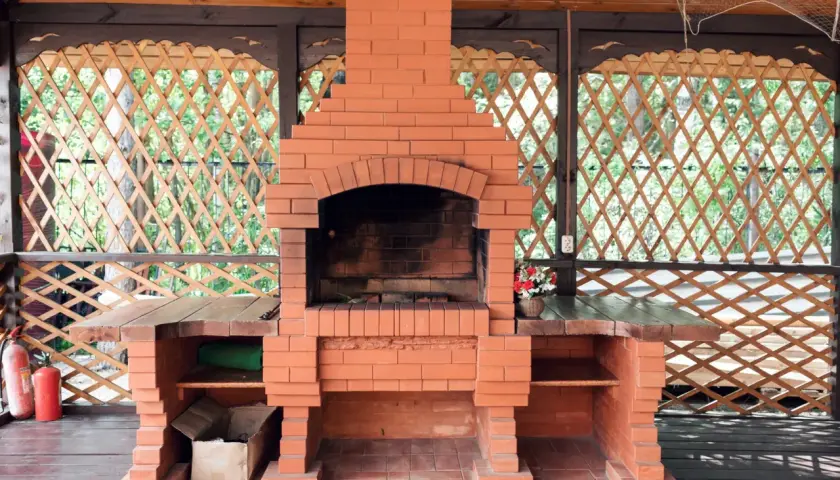 Solidny, prosty grill z cegły w altanie. Obok dwa czerwone gaśnice.