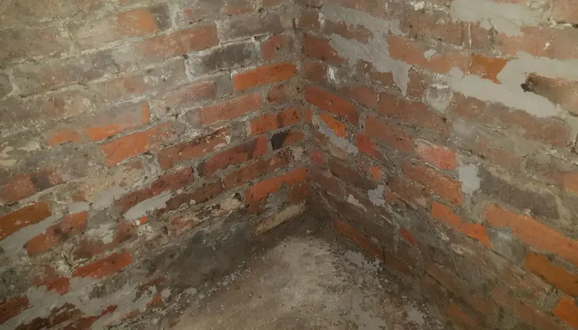 Narożnik piwnicy z ceglanymi ścianami, widoczne ślady prac związanych z hydroizolacją piwnicy od wewnątrz.