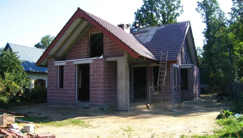 Budowa domu w toku, widoczne materiały budowlane i drabina. Może to być podstawa do obliczenia kary za samowolę budowlaną.