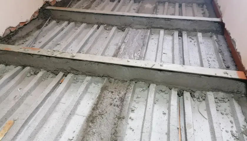 Prace nad tym, jak wzmocnić strop w starym domu. Widoczne betonowe belki i metalowe wsporniki, przygotowywane do dalszych prac budowlanych.