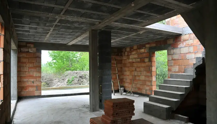 Budowa domu w toku. Widoczny strop z pustaków, schody betonowe, ściany z cegły. Strop co to? To konstrukcja nośna oddzielająca kondygnacje.