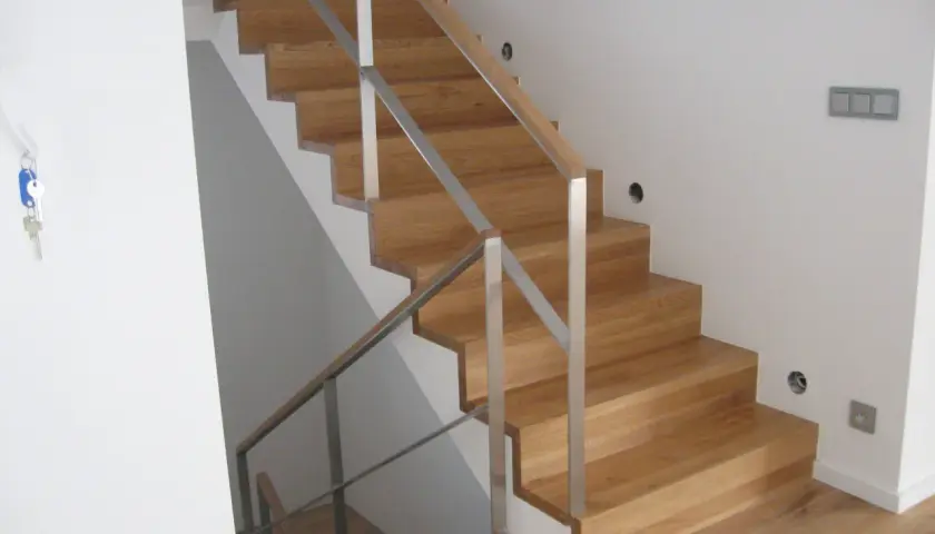 Nowe schody dywanowe na beton, z drewnianymi stopniami i metalową balustradą, tworzą eleganckie i nowoczesne wnętrze.