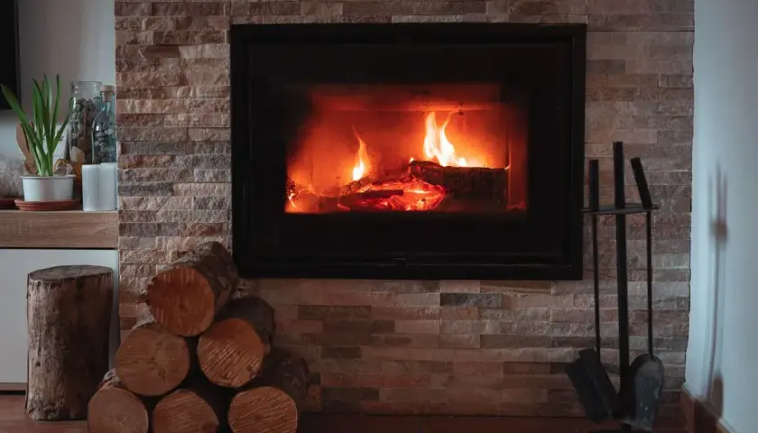 Płonący kominek z drewnem, stos drewna i akcesoria kominkowe.