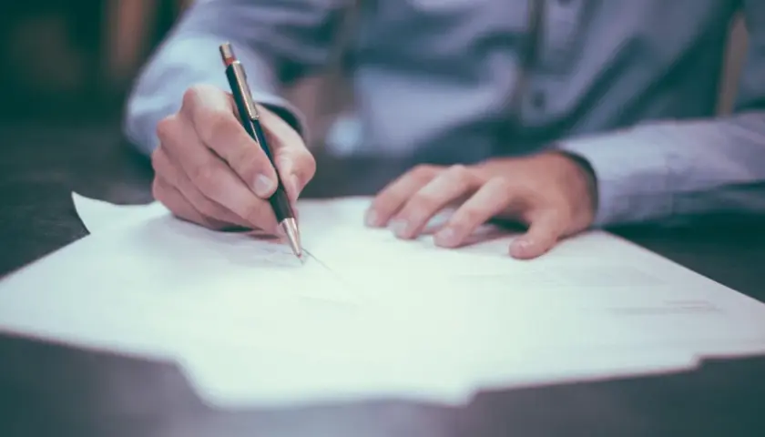 Podpisanie umowy przedwstępnej sprzedaży działki z zadatkiem. Dłoń pisze piórem na dokumencie.