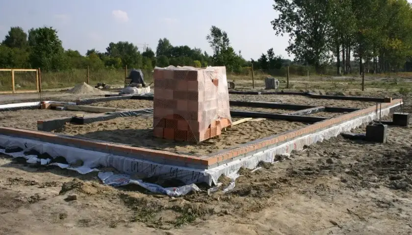 Fundamenty budynku w stanie zero, z widocznymi zarysami ścian i stosem cegieł.