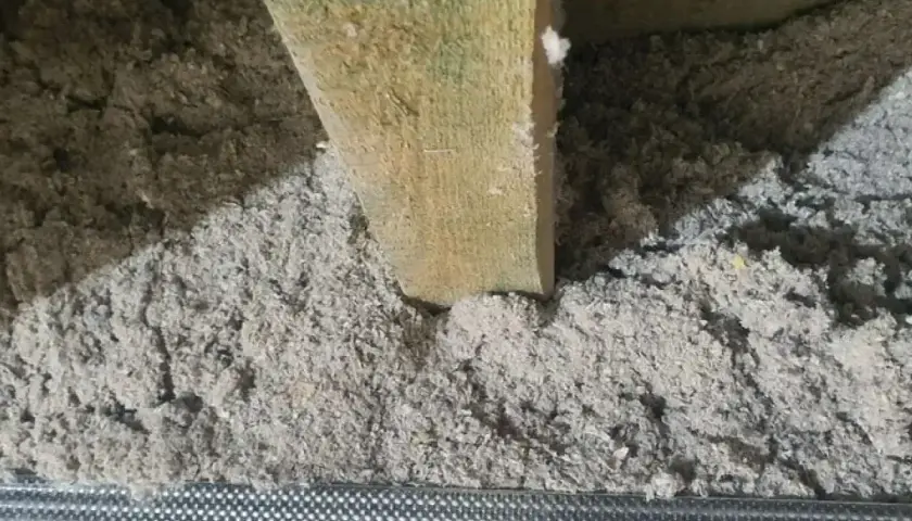 Luźna celuloza w szczelinach, drewniana belka i metalowa siatka. Wady ocieplenia celulozą widoczne przez nierównomierne rozłożenie materiału.