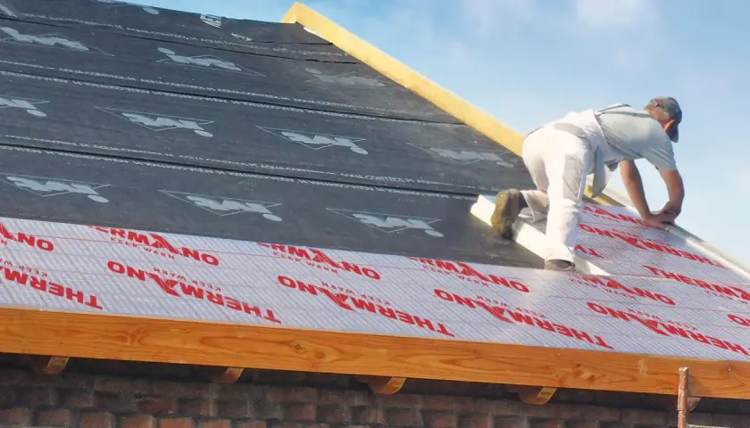 Ocieplenie dachu od zewnątrz. Pracownik montuje izolację "THERMANO" na konstrukcji dachu.
