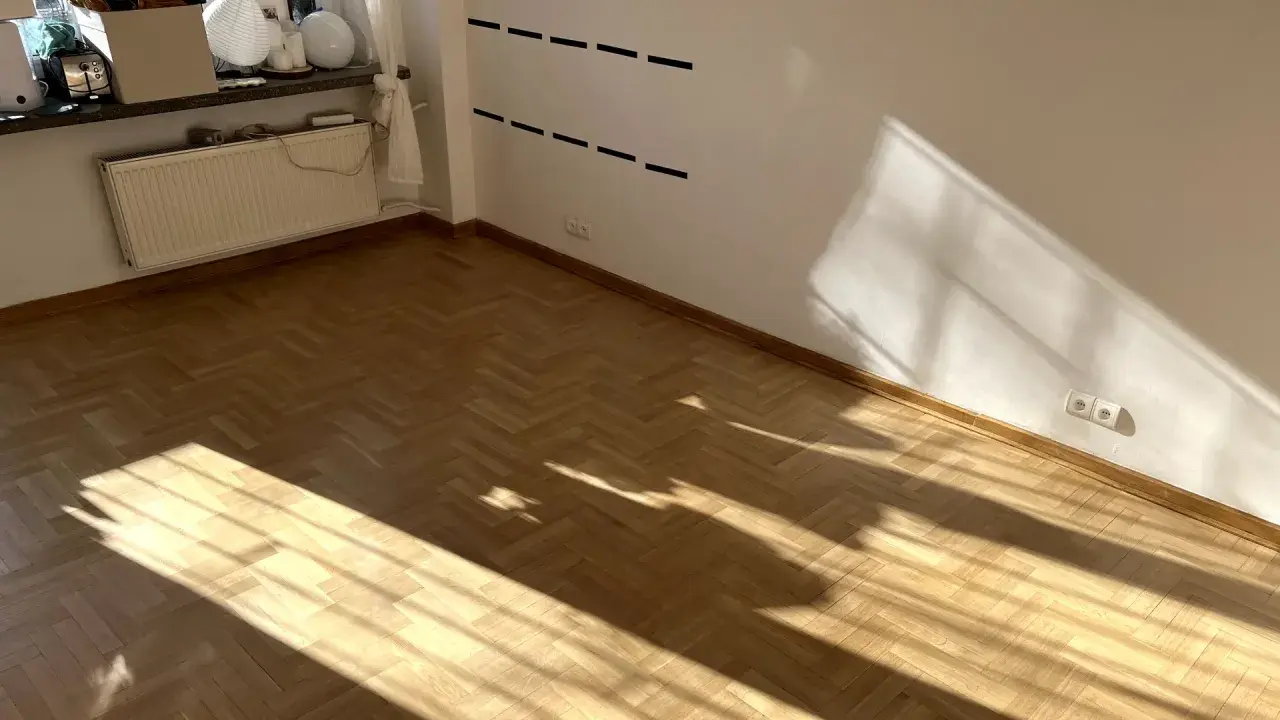 Jasne, drewniany parkiet w jodełkę i białe ściany. Brak listew przypodłogowych, co daje nowoczesny wygląd.