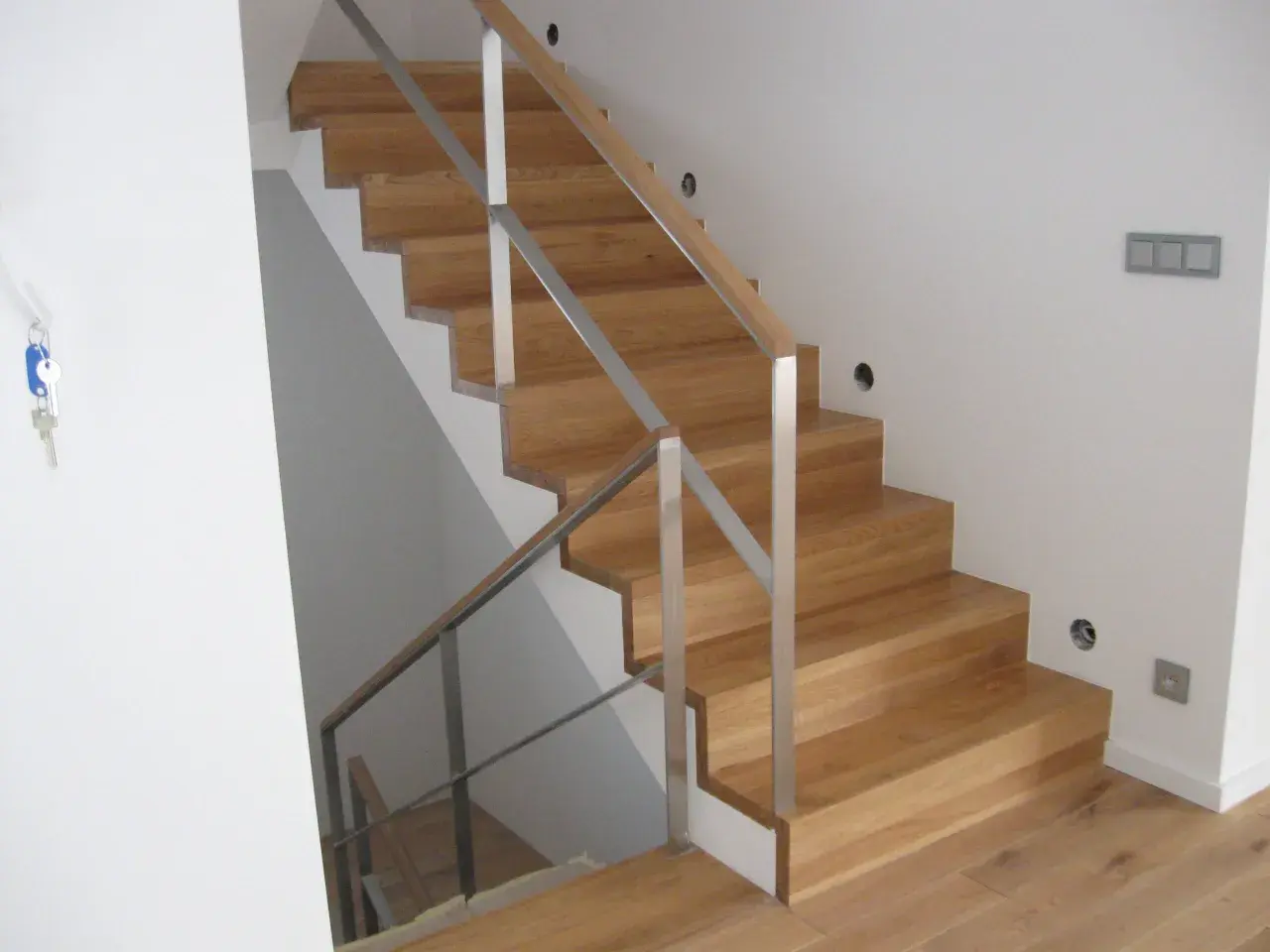 Nowe schody dywanowe na beton, z drewnianymi stopniami i metalową balustradą, tworzą eleganckie i nowoczesne wnętrze.