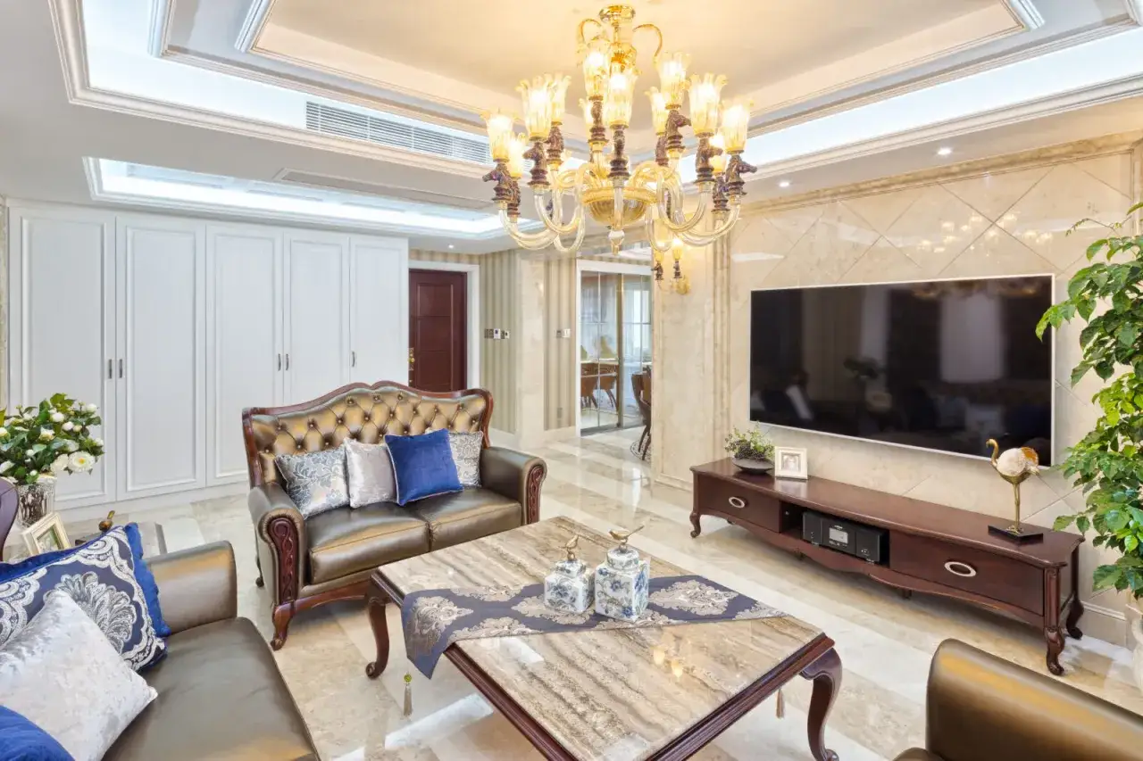 Elegancki salon w stylu glamour: skórzane kanapy, marmurowe akcenty, kryształowy żyrandol i bogate zdobienia.