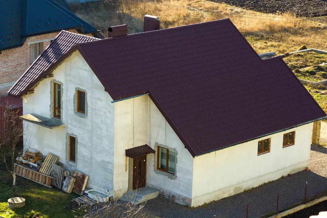 Dom w trakcie budowy na gruntach rolnych zabudowanych. Ciemnobordowa dachówka, białe ściany, drewniane okna.