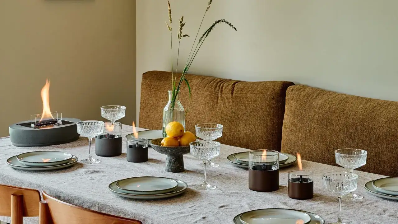 Stół nakryty do kolacji w stylu hygge wnętrza. Płonący kominek, świece, kieliszki i cytryny tworzą przytulną atmosferę.