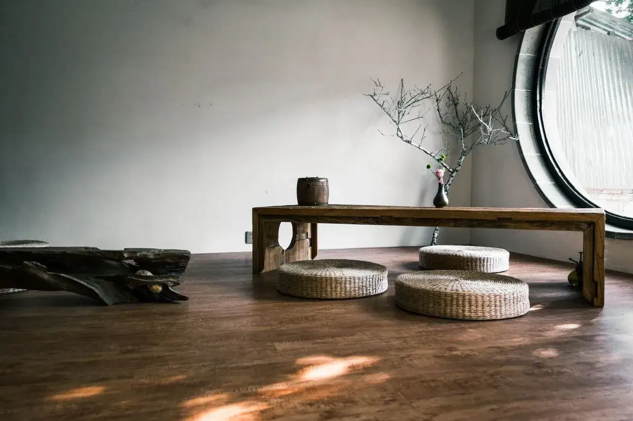 Minimalistyczne wnętrze z drewnianą ławą, okrągłymi poduszkami i gałęzią w wazonie. Inspiracja 55 zasadami feng shui.